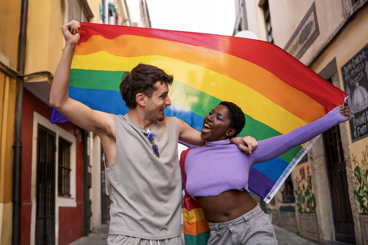 Two people celebrating with a rainbow Pride flag in a sunlit street